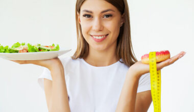 Diet concept, woman measures weight on electronic scales while holding calorie donut.